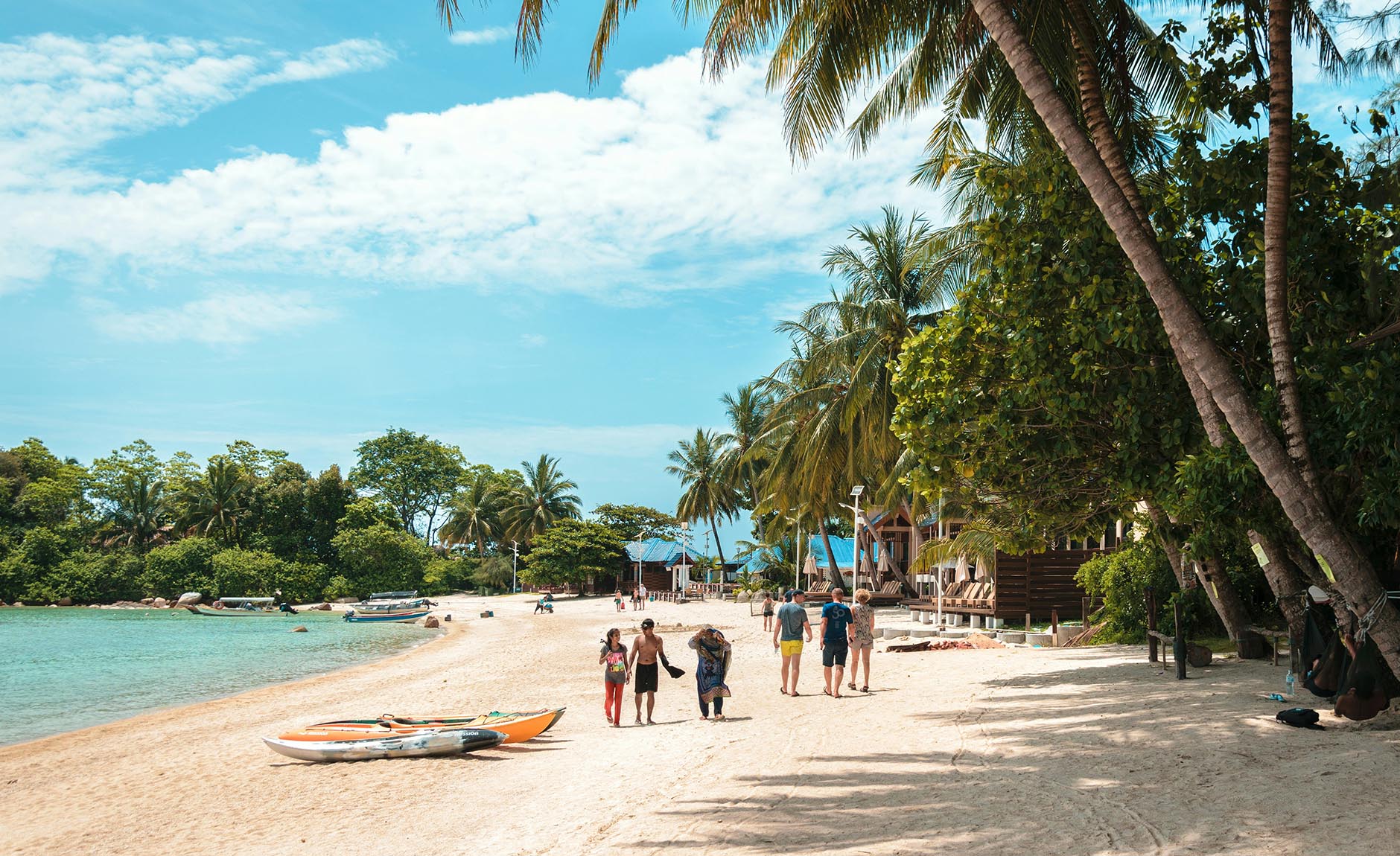 Palm-fringed white sand beach with traditional wooden bungalows in Thailand